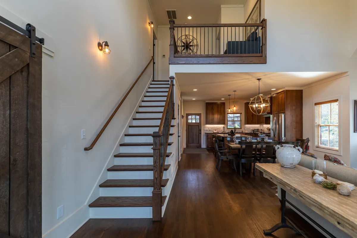 Featuring a prominent staircase, kitchen, and dining area with a large wooden table, this image emphasizes the home's modern rustic décor. The space is inviting and open, ideal for entertaining, family gatherings, or simply enjoying a leisurely coffee while taking in the surroundings from inside.