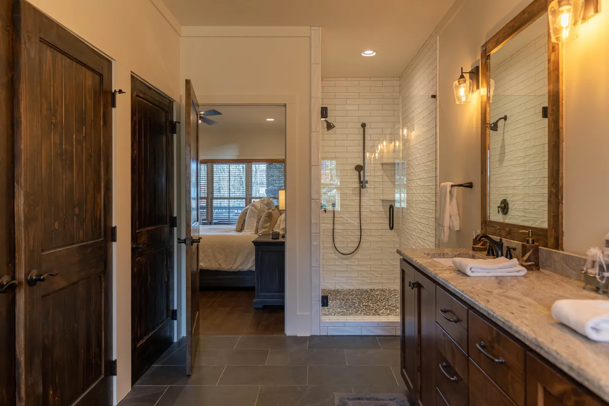 This image showcases a spa-like bathroom with double sinks, a walk-in shower, wooden cabinets, and large mirrors. Its calming mood underscores the luxury of the lodge, offering guests a serene space for personal relaxation and self-care after outdoor adventures.