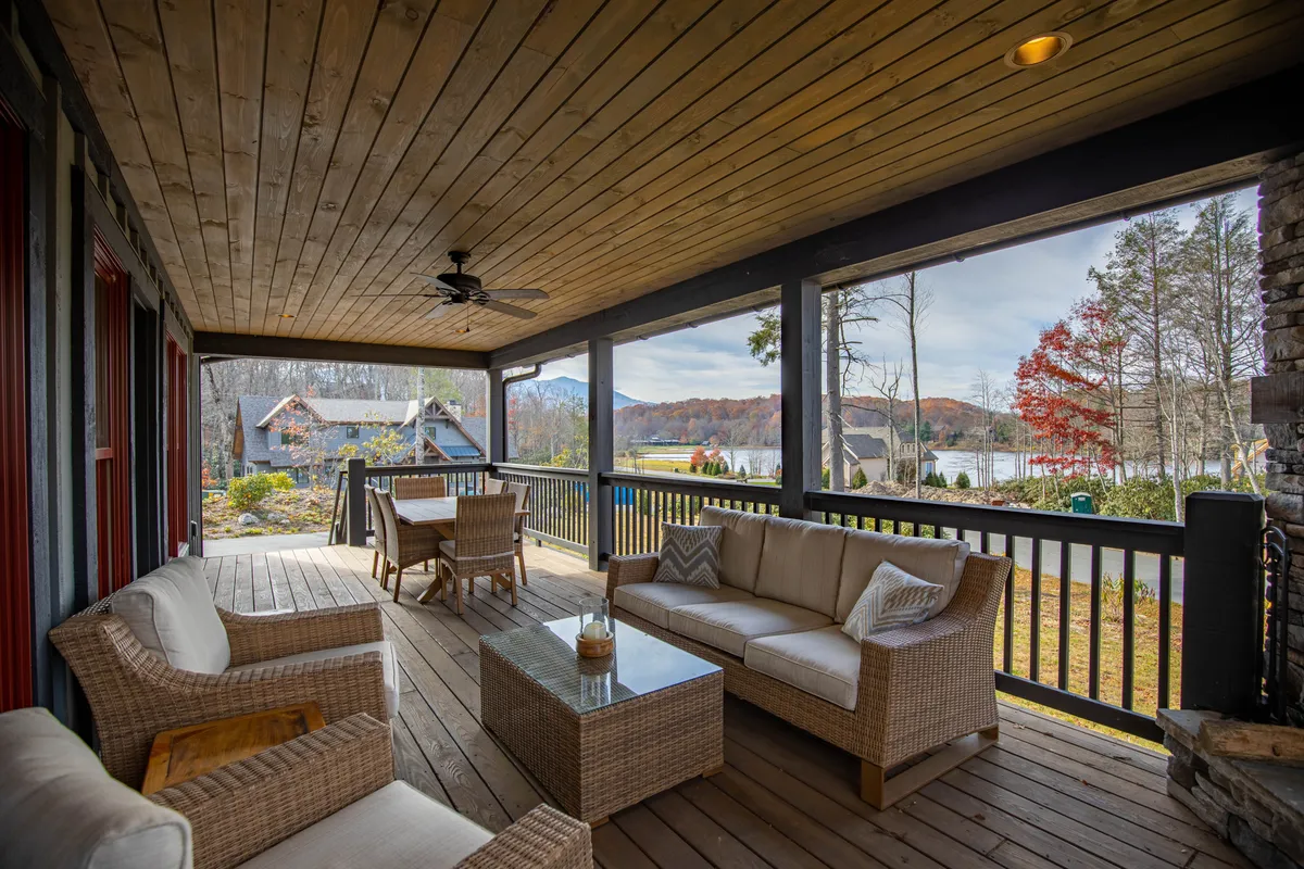 This image shows a comfortable outdoor seating area on a covered deck, overlooking a tranquil lake. Decorative throw pillows and a wooden ceiling bring warmth and comfort to the space, inviting guests to relax, sip coffee, or watch the sunrise. The expansive view and cozy setup are ideal for both quiet mornings and lively gatherings.