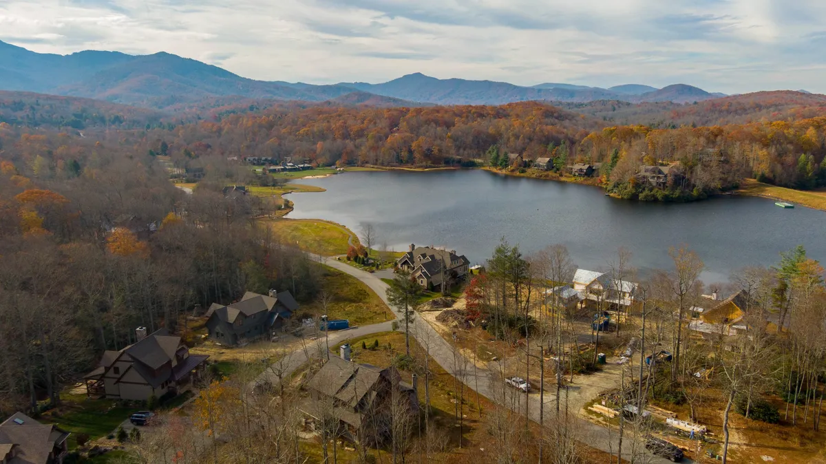 A wide-angle view of the lake framed by mountains and houses, with brilliant autumn foliage and families enjoying the shore. The image suggests accessibility, community interaction, and the recreational use of the natural surroundings.