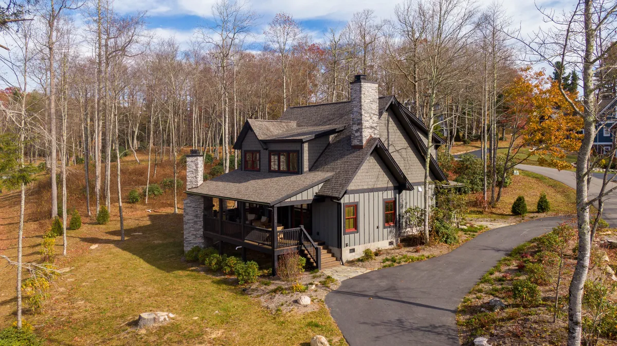 The image showcases a charming single-family home with a striking stone chimney, a spacious porch perfect for relaxation, and a lush wooded landscape that surrounds the property, evoking a sense of seclusion and tranquility. The inviting porch hints at cozy gatherings, while the natural setting suggests opportunities for outdoor adventure and quiet moments amidst the trees.