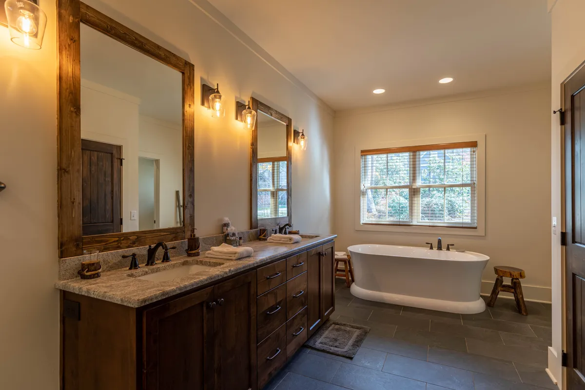 A spa-like bathroom with a freestanding soaking bathtub, double vanity, large mirrors, and ample natural light streaming through windows. The atmosphere is serene and luxurious, ideal for relaxation and self-care.